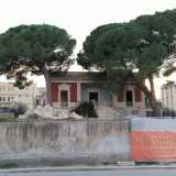 Siamo di fronte al muro perimetrale dell�edificio. Un tempo segnato da un sontuoso ingresso, oggi � chiuso dalla recinzione dei lavori in corso che lasciano comunque intravedere la facciata rossa e bianca della villa...